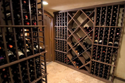 Wine cellar with various built-in shelving and light tan tile floors.