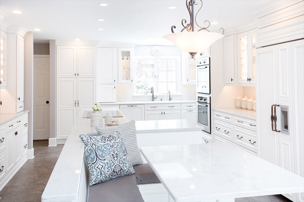 Classic white, light & bright kitchen with stone-top white table with bench seating, and recessed lighting.