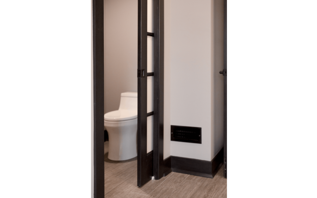Remodeled primary suite with pocket door mostly open, leading to en-suite bathroom with wide doorway and comfort-height toilet.