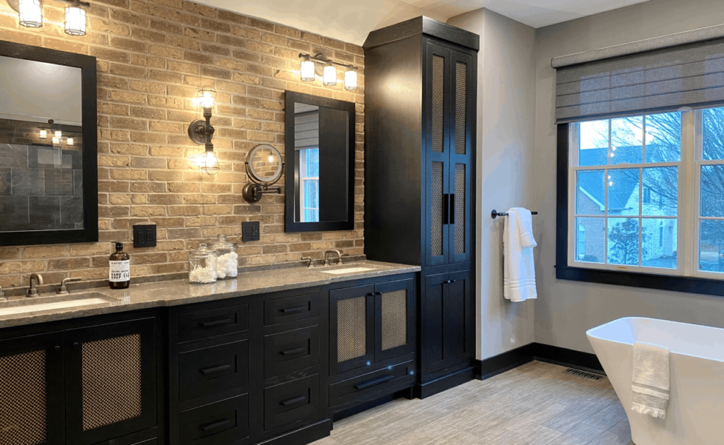 Remodeled primary bath with tan brick wall, dual vanity, and black cabinetry. Soaking tub and large window on the right.