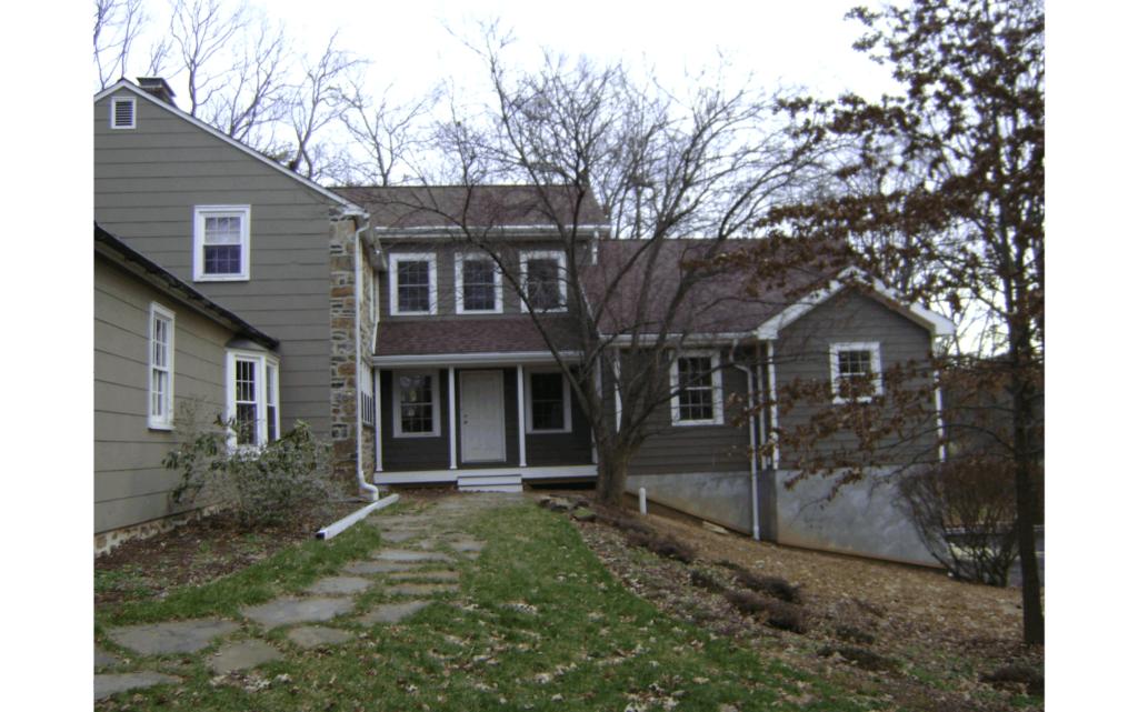 Two-story home with gray-green siding and an addition built onto the right side. Stone path leading to front door.