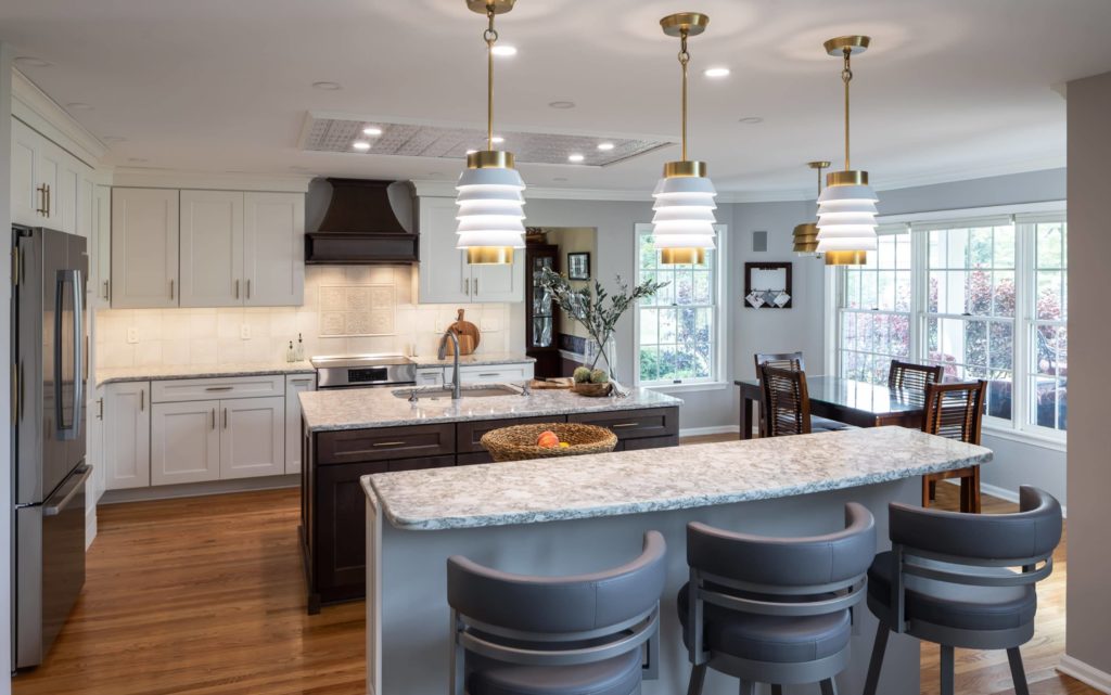 Kitchen remodel with a double island, stone countertops, pendant lights, and white cabinetry