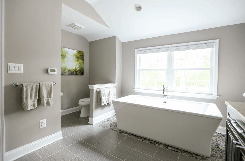 Remodeled bathroom with stand-alone tub under a window. Light gray tile floors, light gray walls.