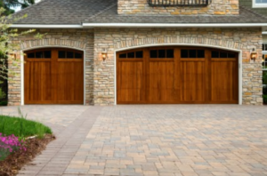 Garage addition outside view. Wood-grain garage doors with small windows in  the top, on a tan brick home.