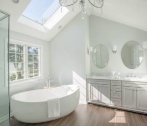 Bathroom remodel with skylight in high ceilings, stand-alone soaking tub, and wood floors.
