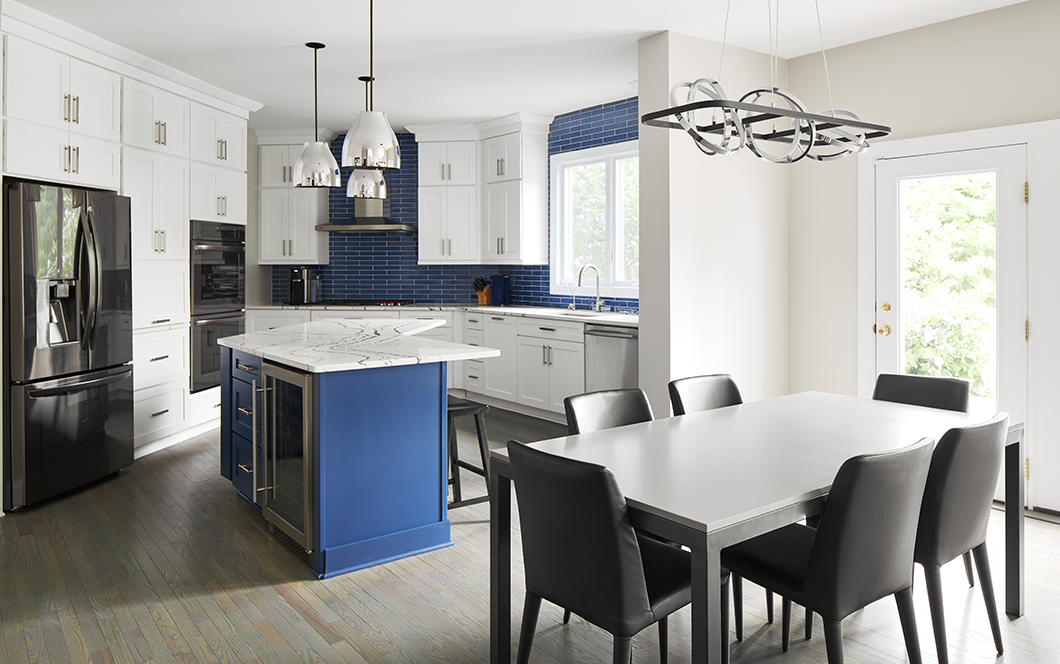 A custom kitchen redesign with blue cabinet and tiling accents and a white dining table with black leather chairs.