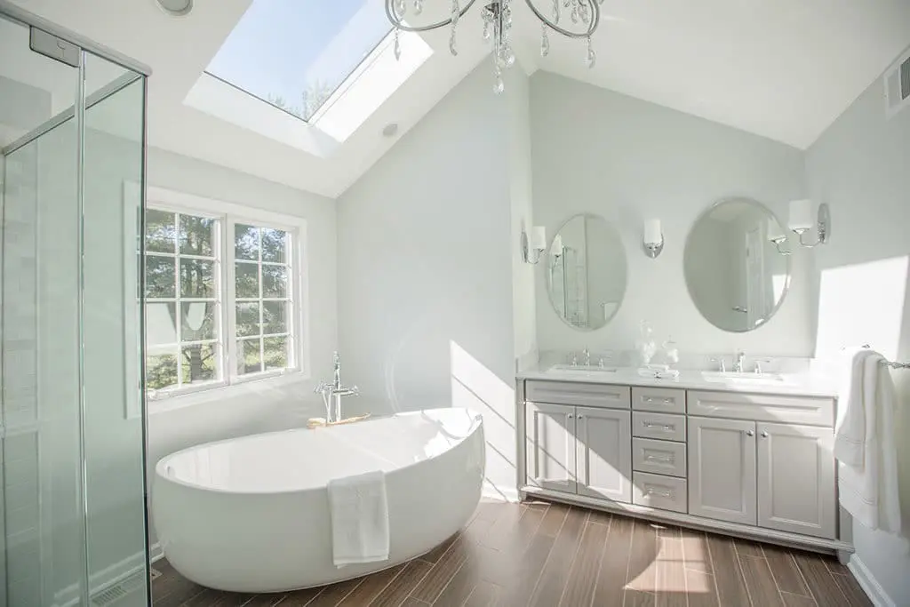 Luxurious white bathroom remodel with skylight, free-standing bathtub and crystal chandelier