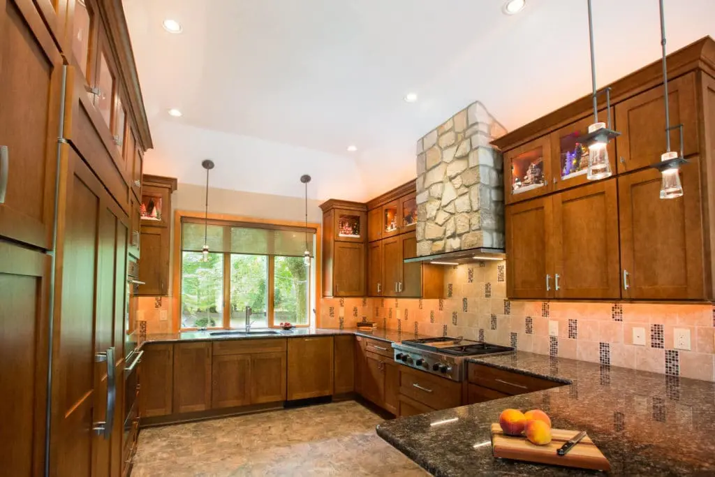 Warm wood kitchen remodel with floor to ceiling cabinets and a stone tile stove hood.