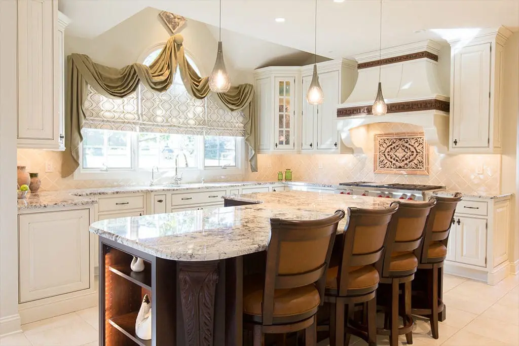 Elegant kitchen remodel with white cabinets and intricate dark wood carving accents, an L shaped island.