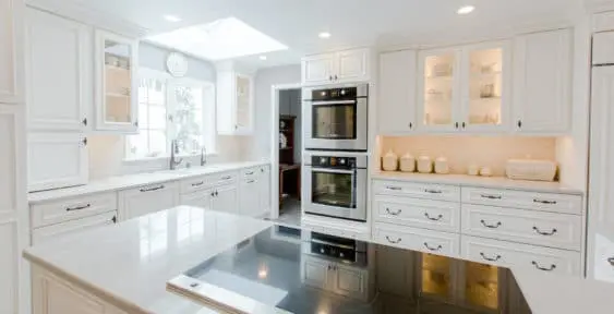 White kitchen remodel with double ovens on far wall and electric flat stovetop in foreground.