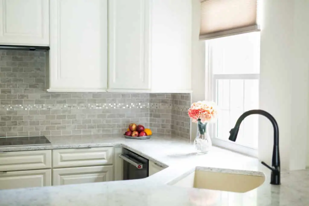 White kitchen remodel with a window and grey tiled backsplash.