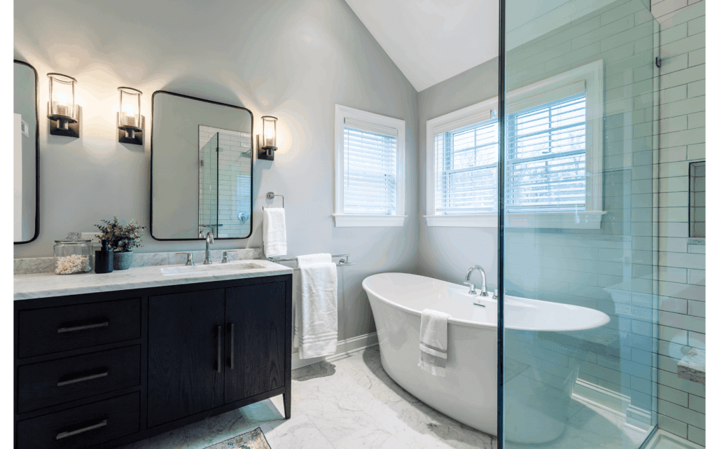 A contemporary-style bathroom with white marble floors, black vanity with white stone countertop, and large white soaking tub to the right. Light gray walls.