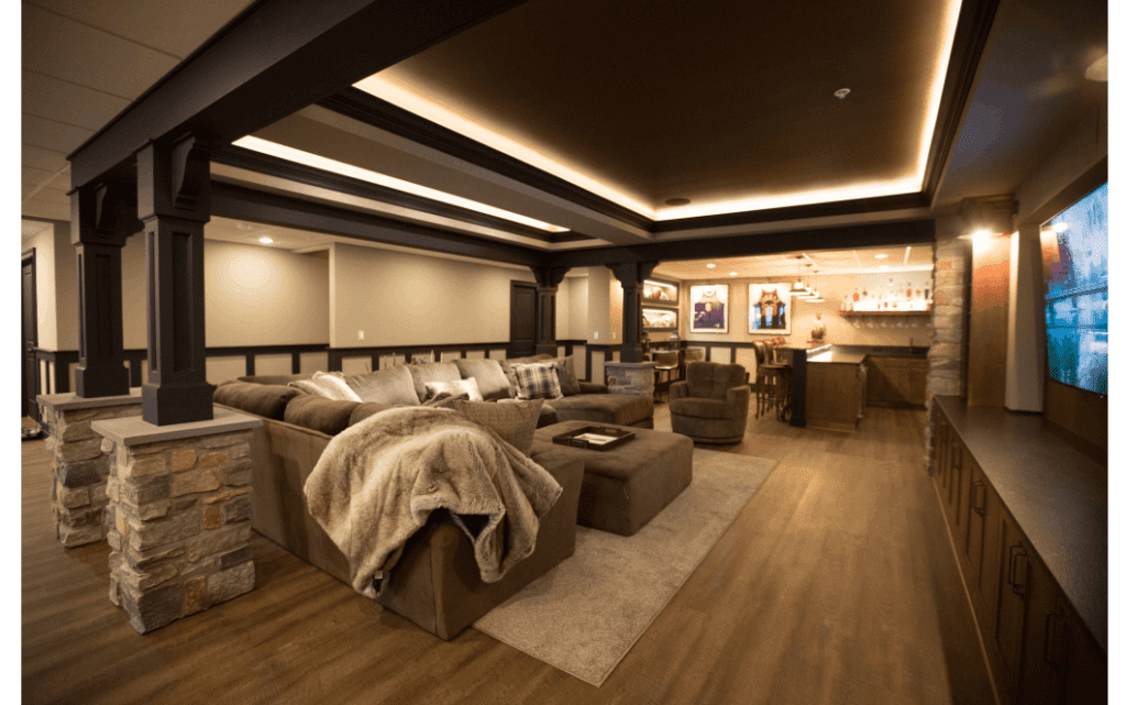 Finished basement remodel with black woodbeam ceiling accents. Wood floors and large sectional couch in middle.