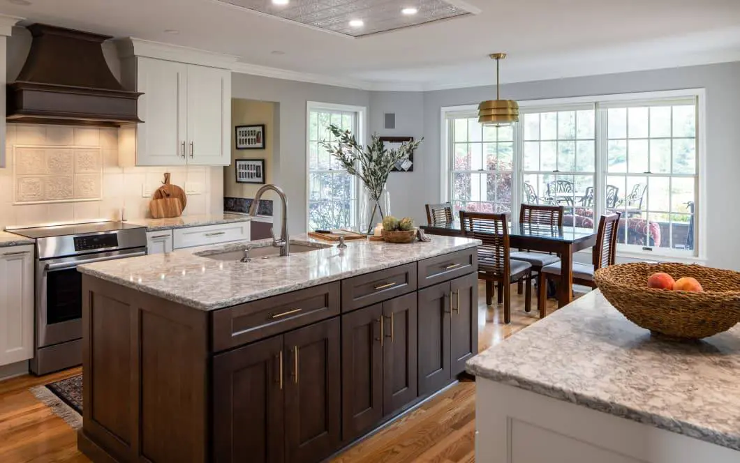 Updated grey kitchen cabinetry with contrasting dark wooden island and custom range hood