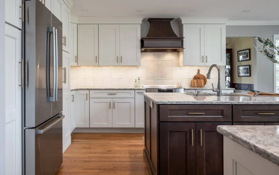 Updated grey kitchen cabinetry with contrasting dark wooden island and custom range hood