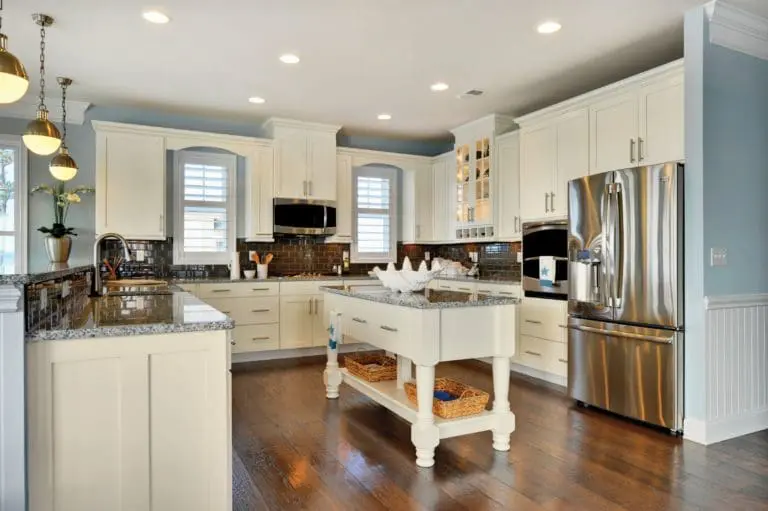 Kitchen remodel with wood floors, white traditional-style cabinets, granite countertops, dark tile backsplash, small island in the middle, and recessed lighting.