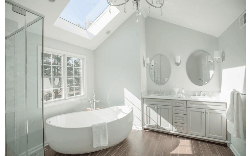 Bright vaulted primary bathroom with double vanity sinks, large freestanding tub, and skylight.