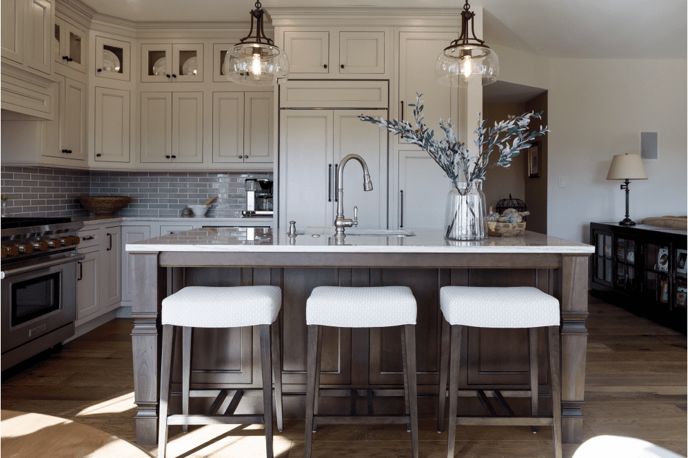 Modern cozy kitchen remodel with white cabinets, an island with three stools along one side, wood floors, two pendant lights over island.