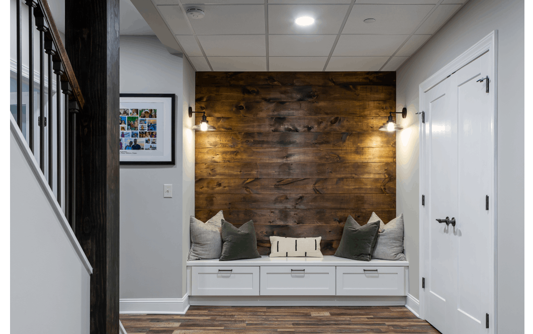Sitting area at the bottom of staircase with custom storage bench and rustic wood-paneled accent wall