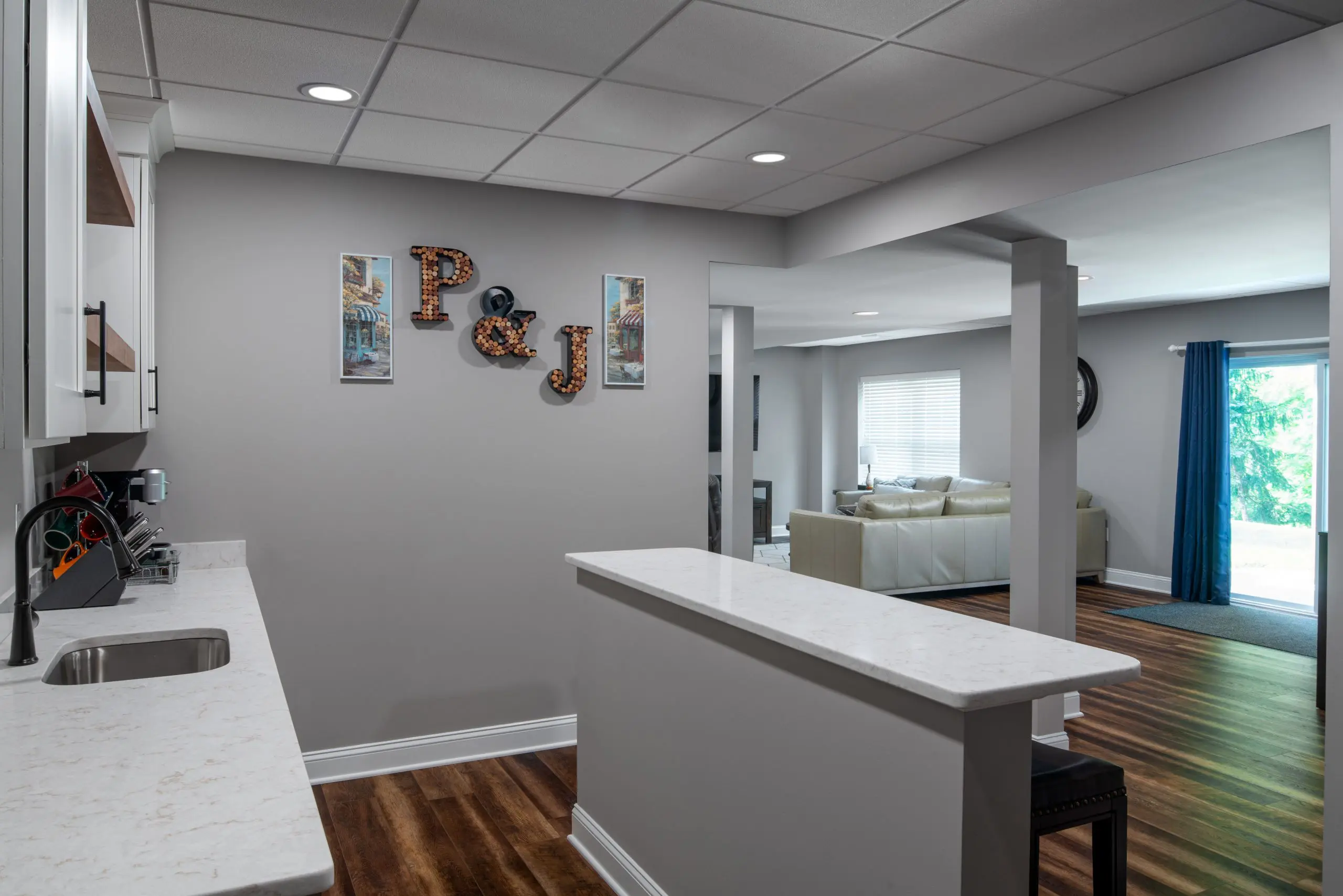 A basement redesign with a sectional, a kitchenette, and bar seating.