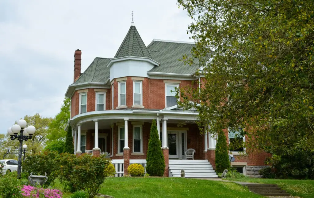 Victorian brick home exterior with wraparound porch, turret, and tall windows.