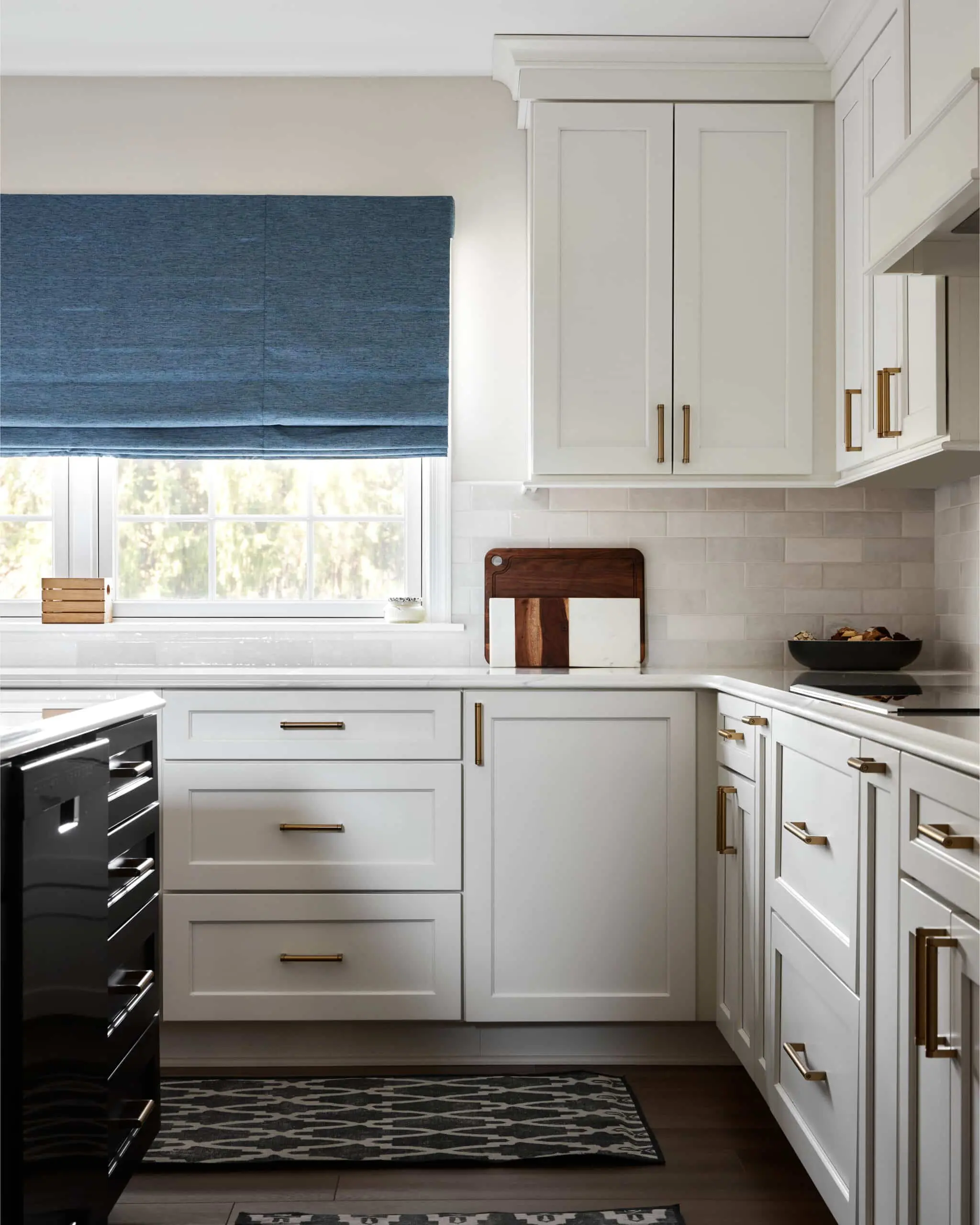 A custom remodeled kitchen with white textured tile backsplash, white cabinets, and gold cabinet handles.