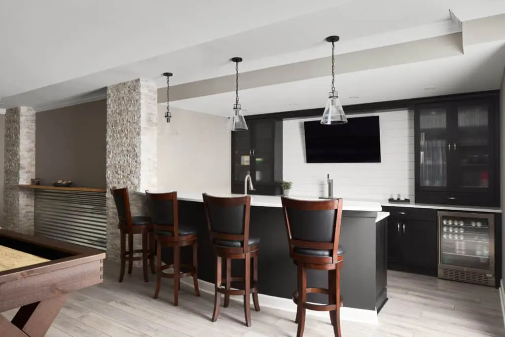Remodeled living space with light wood flooring, black cabinets in bar area with stool seating, TV mounted on wall.