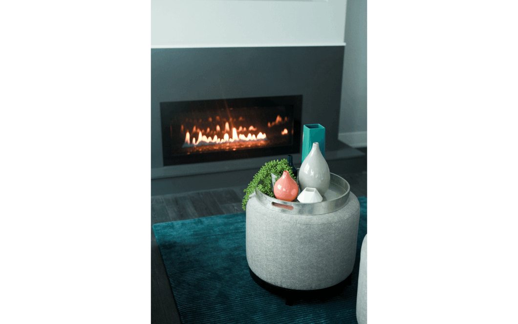 Closeup of modern floating fireplace sitting behind round grey footstool with decorative tray and vases