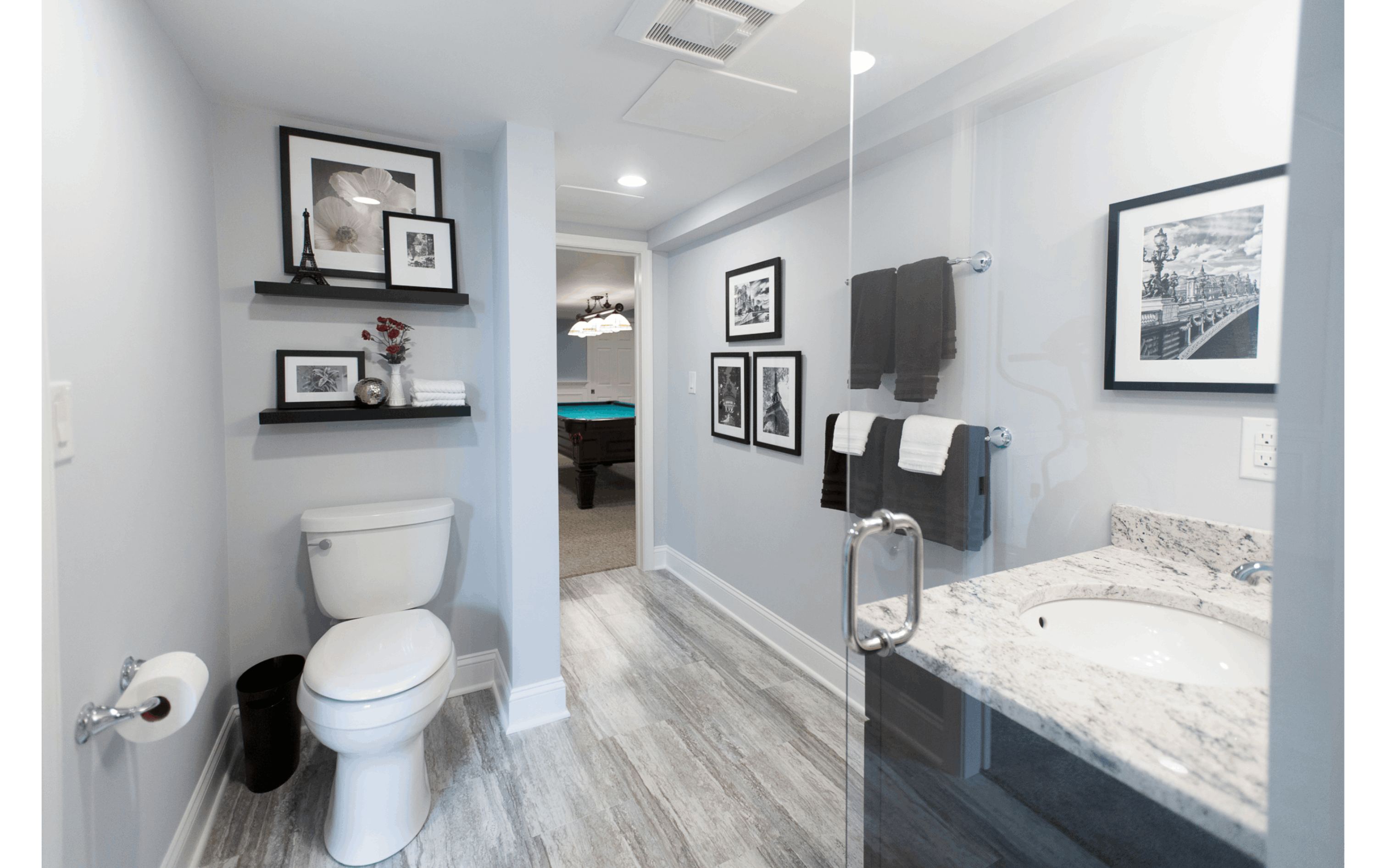 Upgraded basement bathroom with private toilet niche, glass shower and granite vanity, overlooking pool table in the next room