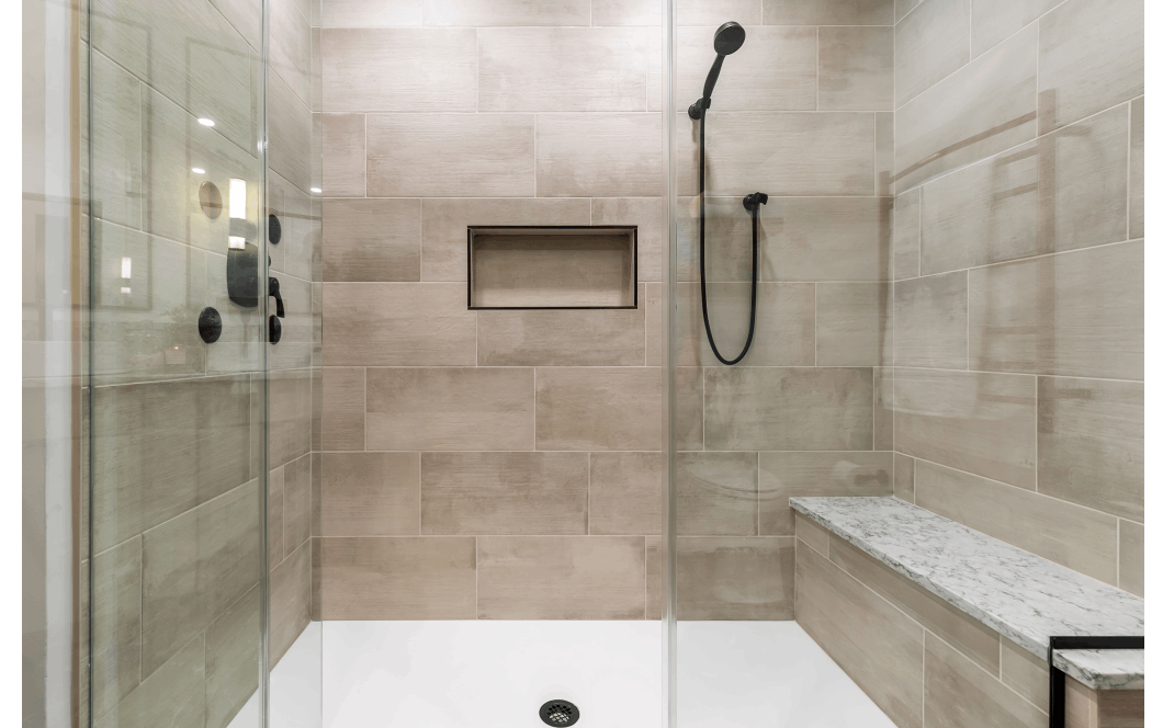 A renovated walk-in shower with tan brushed tile and granite bench.
