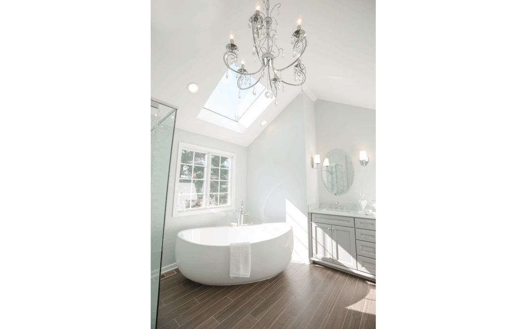 Light and airy vaulted bathroom with skylights, a freestanding tub, and an ornate crystal chandelier
